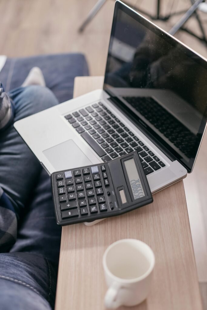 High angle view of a laptop and calculator on a wooden desk with a coffee mug.
